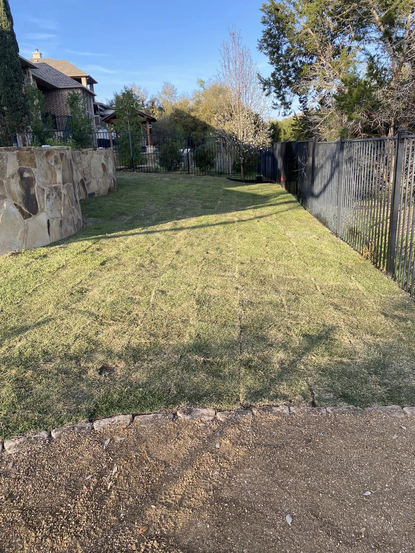 Fresh sod in the side yard beside the stone wall and black iron fence